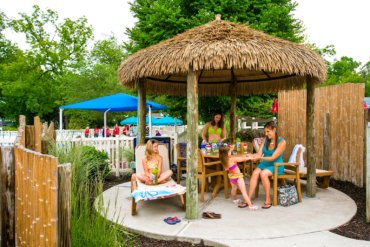 Family sits under a shaded cabana at water play area